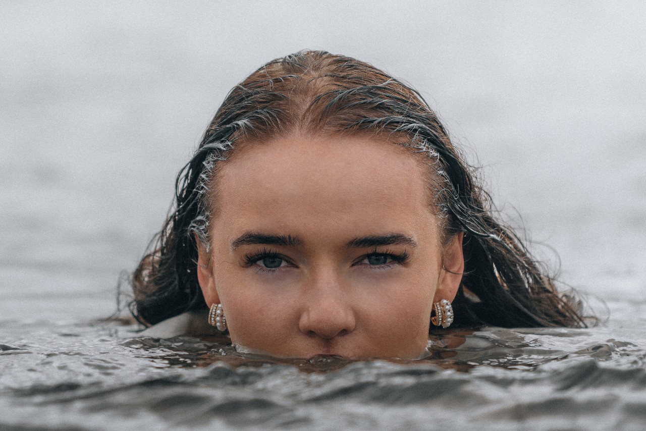 a woman’s face half submerged in water and wearing pearl huggie earrings