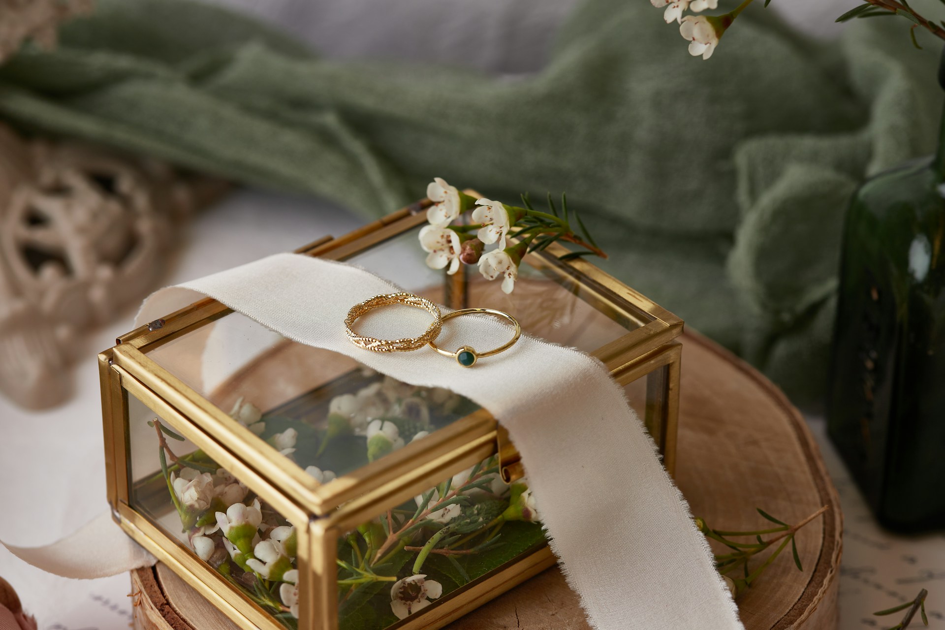 A close up of two thin yellow gold wedding bands on top of a glass box with flowers inside