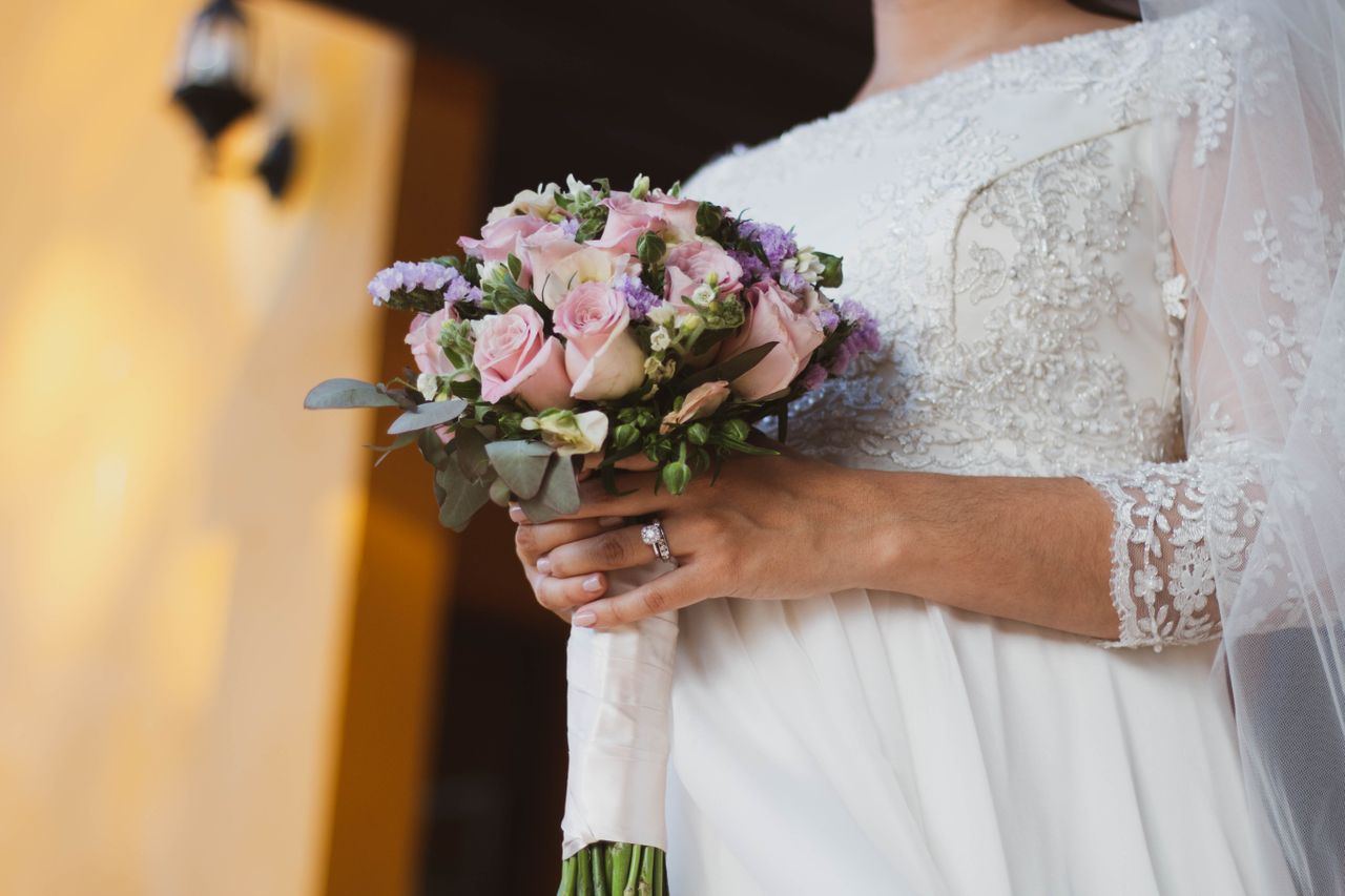 A bride in a lace dress holding a bouquet of flowers, showcasing dazzling white gold bridal set – engagement ring and wedding band.