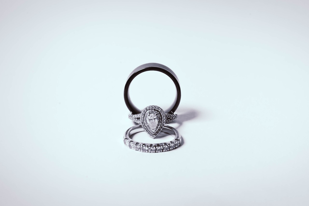 Three rings arranged in a pyramid shape, featuring a plain black band, a diamond-studded band, and a centre pear shaped ring.